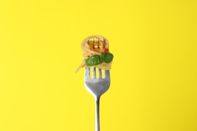 Photo of Fork with tasty pasta, basil and tomato sauce on yellow background