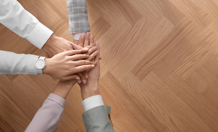 Photo of People holding hands together over wooden background, top view with space for text. Unity concept