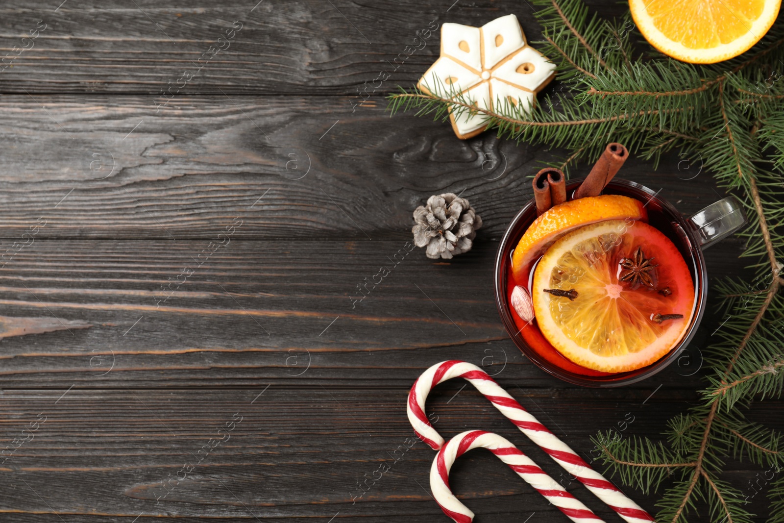 Photo of Glass cup of tasty mulled wine on black wooden table, flat lay. Space for text