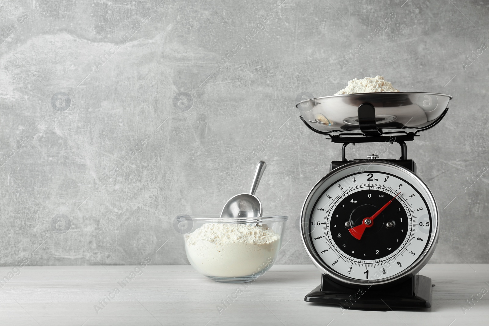 Photo of Kitchen scale with flour on white wooden table. Space for text
