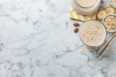 Photo of Glass of tasty banana smoothie with oatmeal on white marble table, flat lay. Space for text