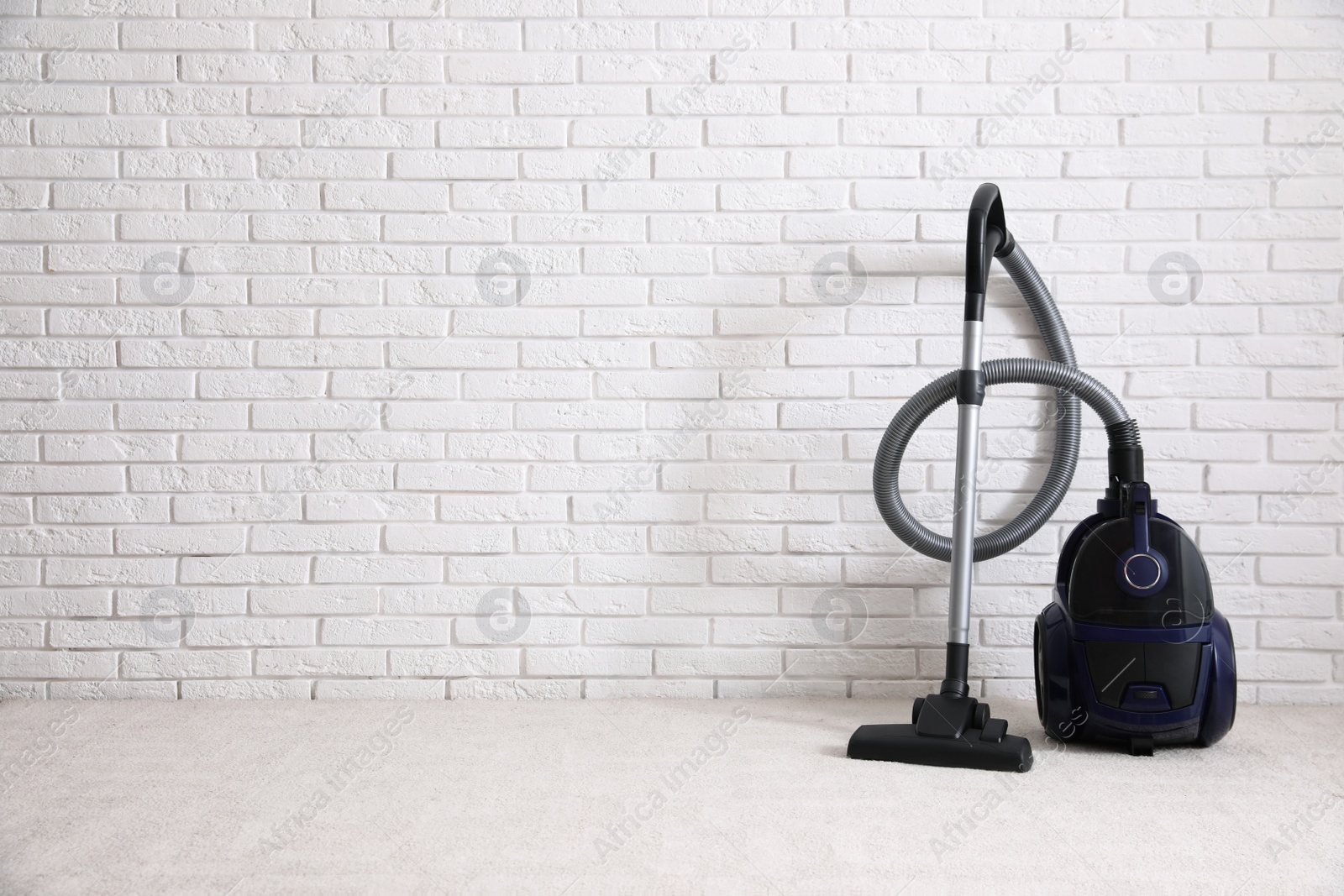 Photo of Modern vacuum cleaner near white brick wall indoors, space for text