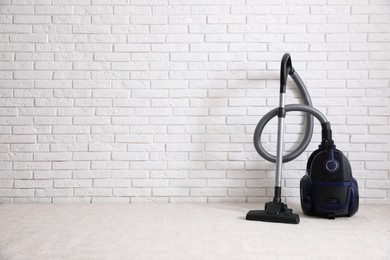 Photo of Modern vacuum cleaner near white brick wall indoors, space for text