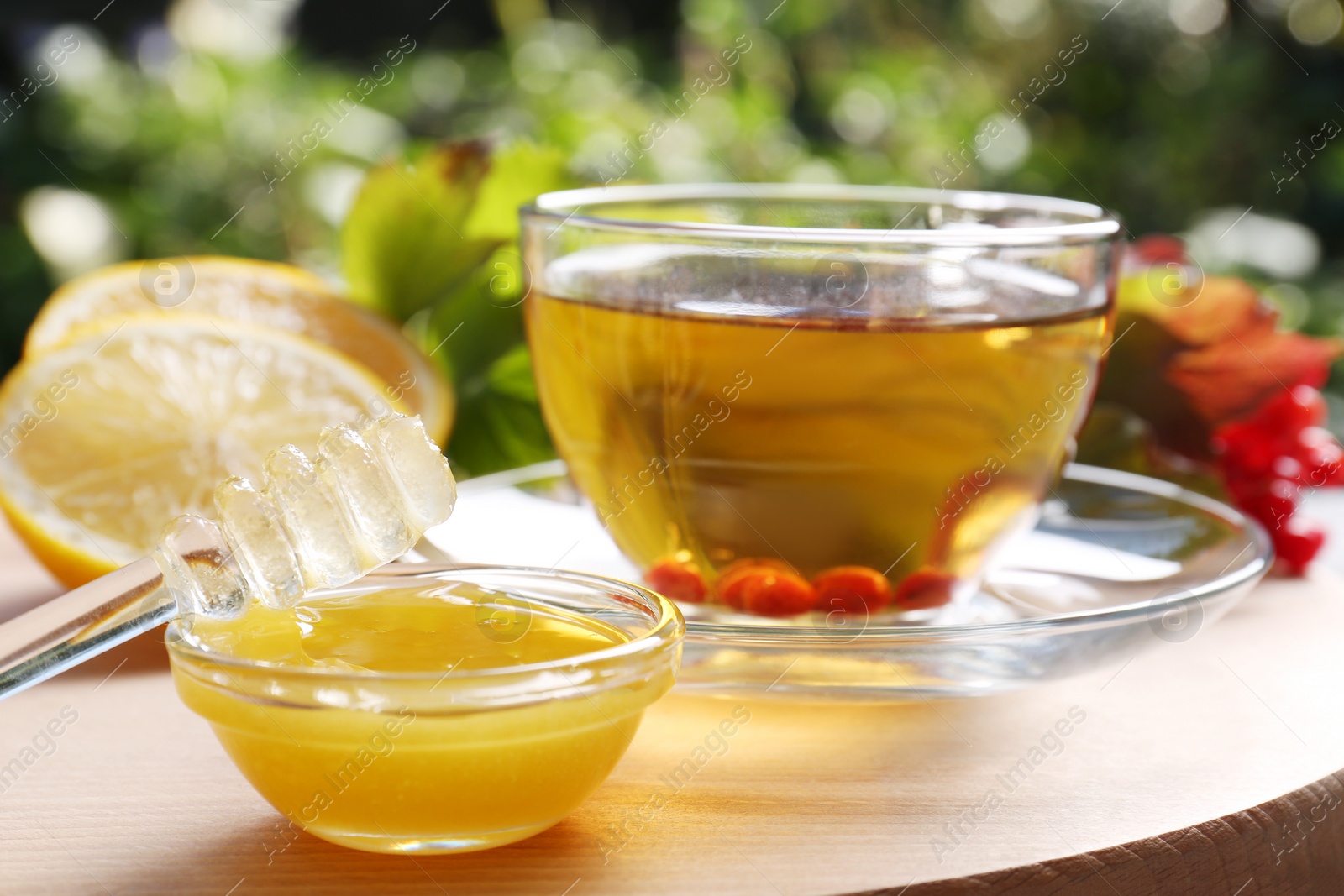 Photo of Bowl and dipper with honey, cup of delicious tea on wooden table outdoors, closeup