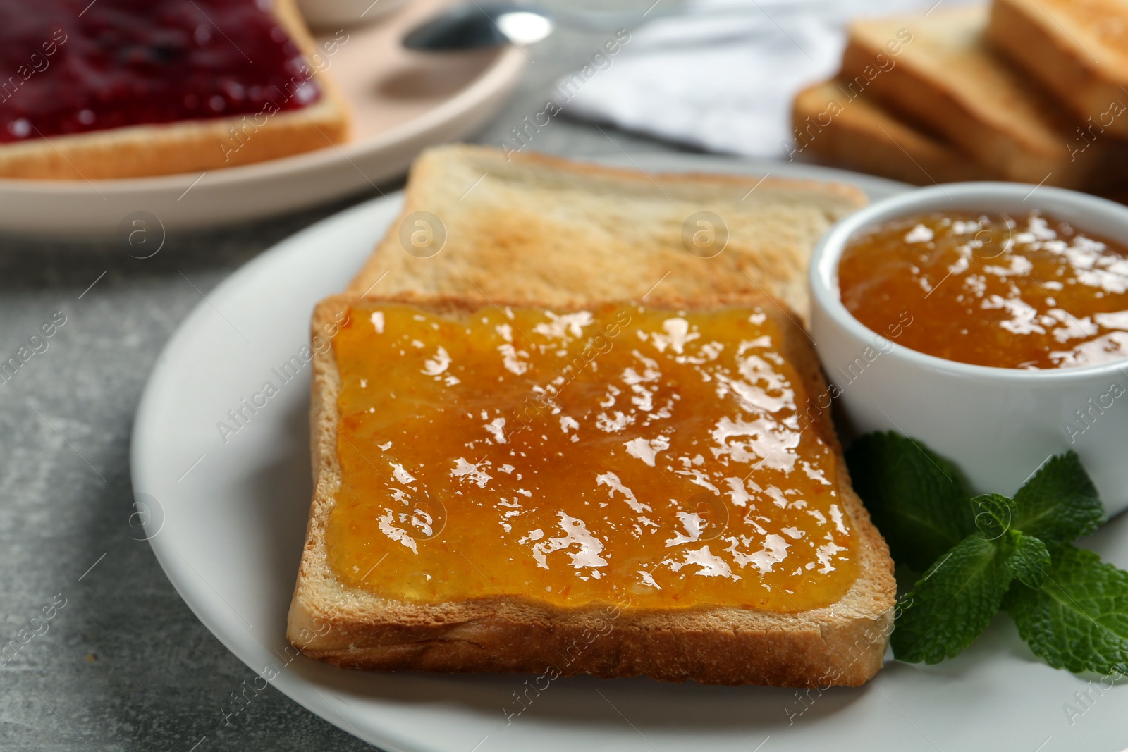 Photo of Delicious toasts served with jam and mint on light grey table, closeup