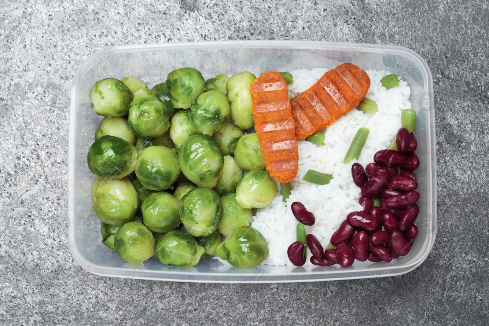 Photo of Tasty rice with cutlets and vegetables in plastic container on grey table, top view