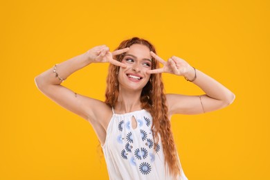 Photo of Beautiful young hippie woman showing V-sign on orange background