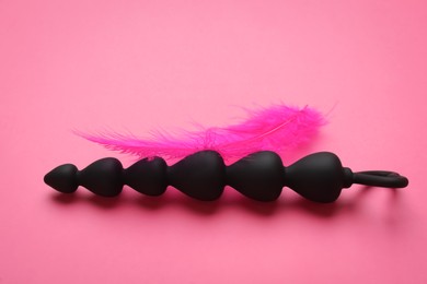 Anal beads and feather on pink background. Sex toy