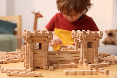 Little boy playing with wooden construction set at table in room, selective focus. Child's toy