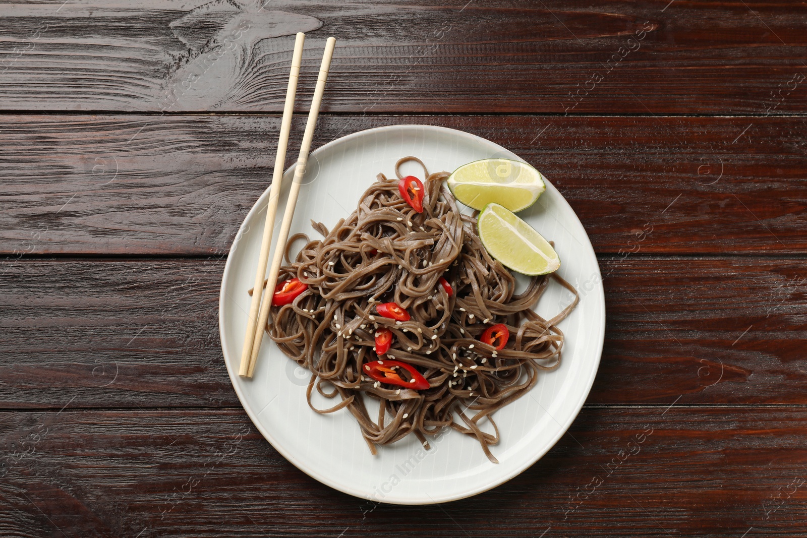 Photo of Tasty buckwheat noodles (soba) with chili pepper, lime and chopsticks on wooden table, top view