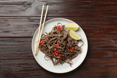 Photo of Tasty buckwheat noodles (soba) with chili pepper, lime and chopsticks on wooden table, top view