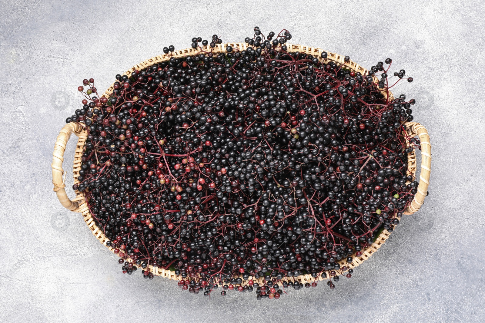 Photo of Wicker basket with ripe elderberries on light grey table, top view