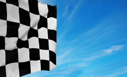 Image of Checkered racing finish flag against blue sky. Space for text