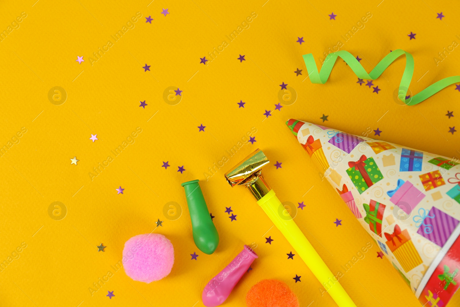 Photo of Bright festive hat and other party accessories on yellow background, flat lay