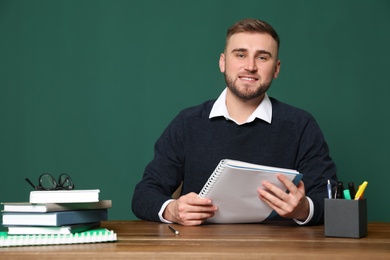 Portrait of young teacher at table against green background. Space for text