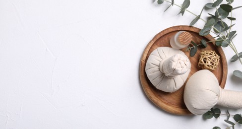 Flat lay composition with herbal massage bags, spa products and eucalyptus branches on white table. Space for text