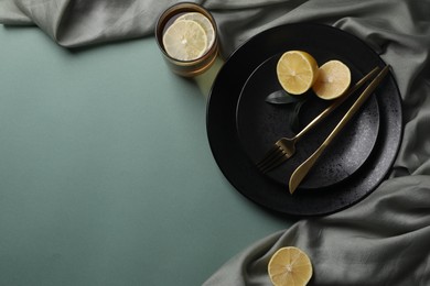 Stylish table setting. Plates, cutlery and tea with lemon on olive background, top view. Space for text