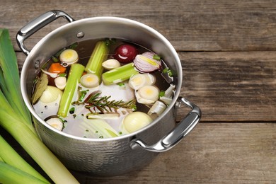 Different ingredients for cooking tasty bouillon in pot and celery on wooden table, space for text