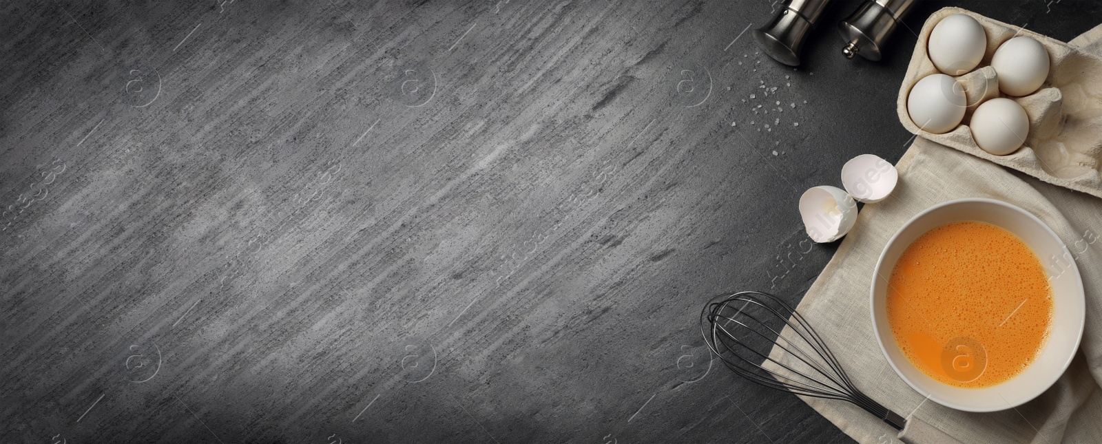 Image of Metal whisk, beaten eggs and shells on dark grey table, top view. Banner design with space for text