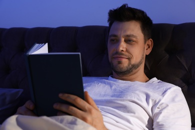 Handsome man reading book in dark room at night. Bedtime