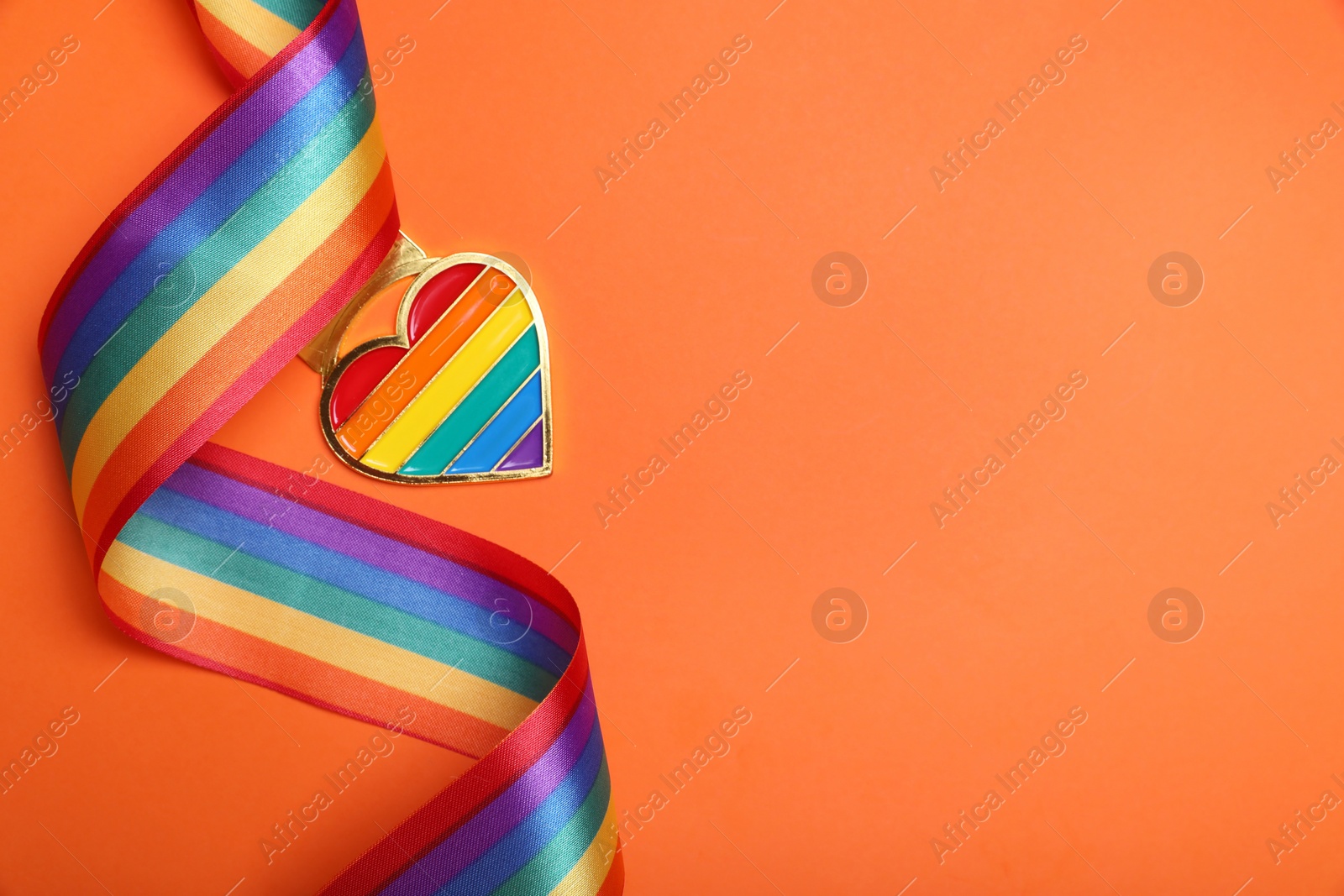 Photo of Rainbow ribbon with heart shaped pendant on orange background, top view and space for text. LGBT pride