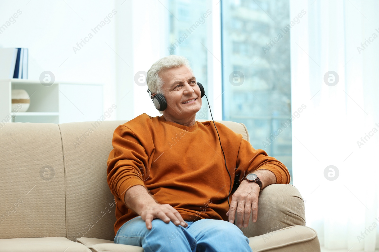 Photo of Portrait of mature man with headphones on sofa indoors