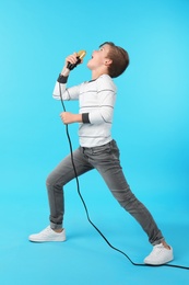 Cute boy singing in microphone on color background