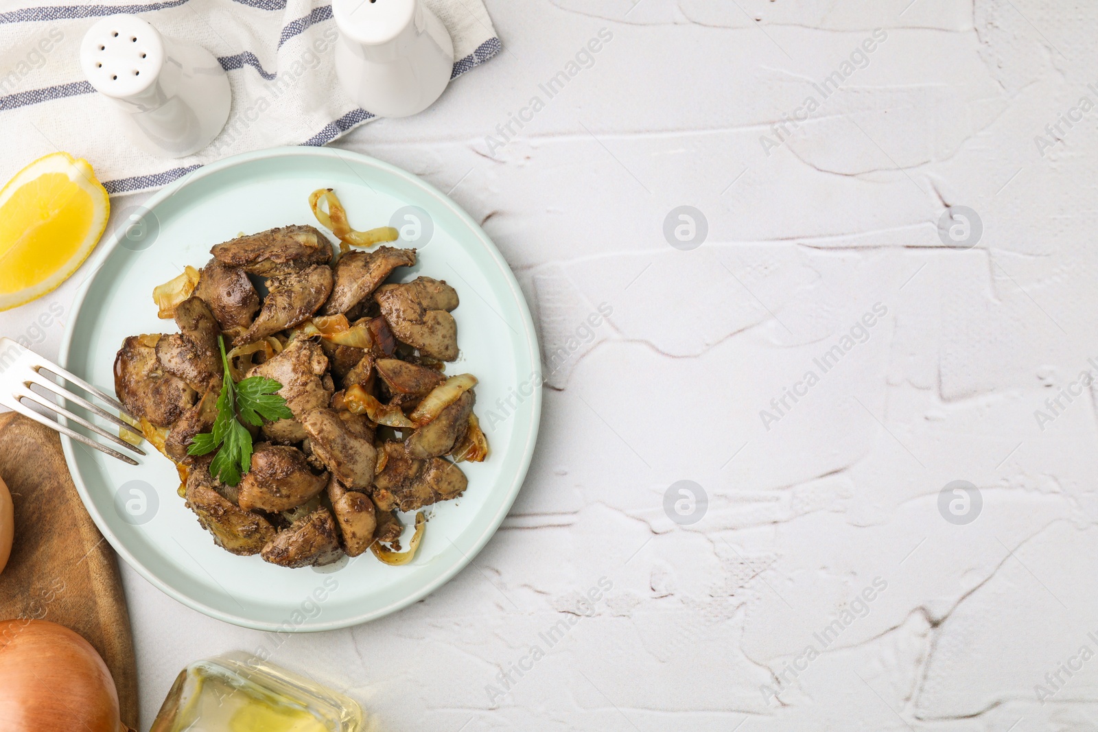 Photo of Tasty fried chicken liver with onion and parsley served on white textured table, flat lay. Space for text