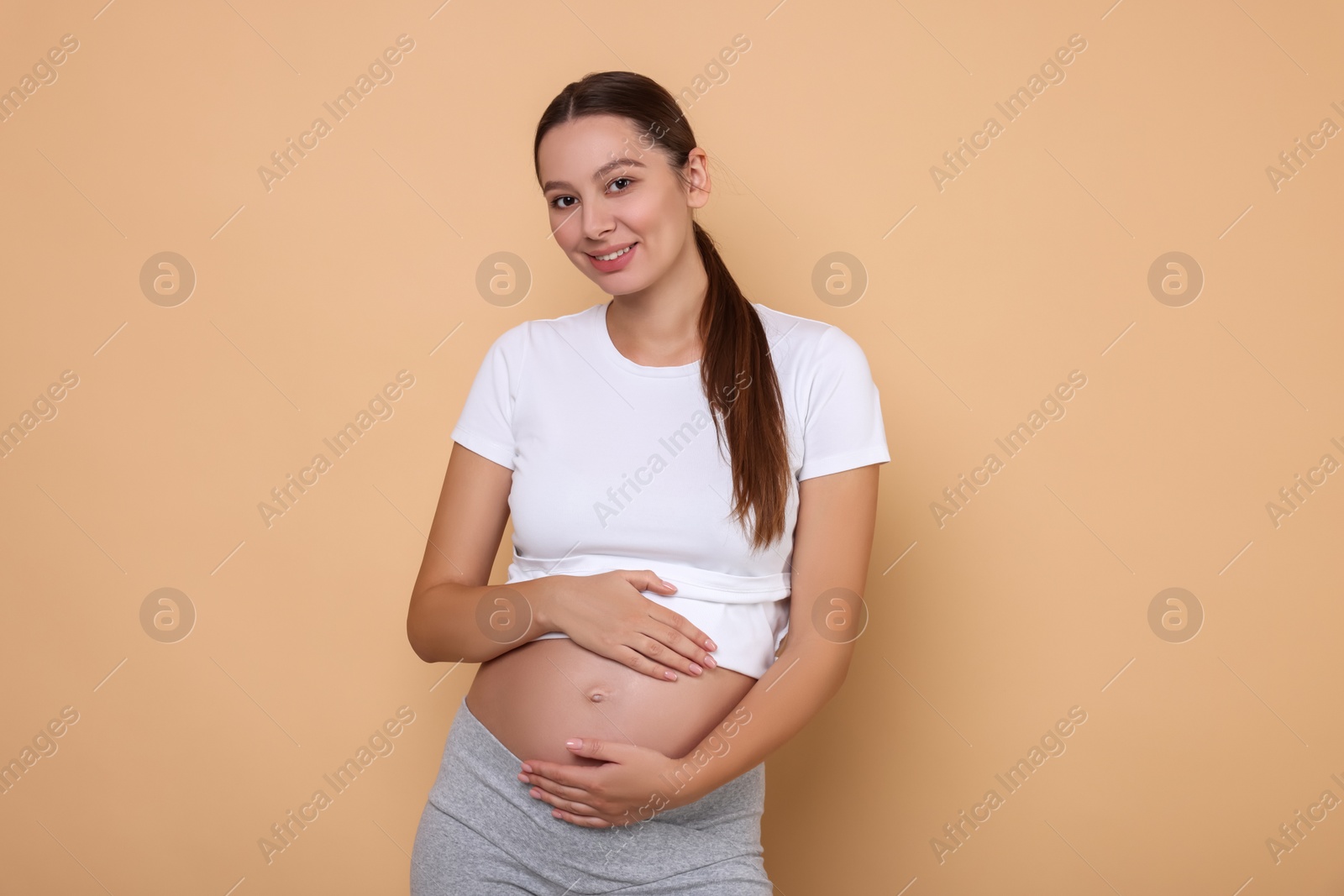 Photo of Beautiful pregnant woman in white T-shirt on beige background