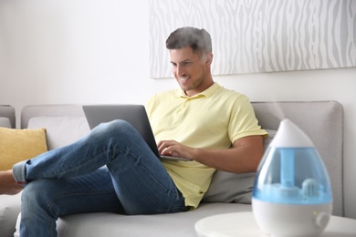 Photo of Man using laptop in room with modern air humidifier