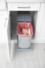 Open cabinet with full trash bin in kitchen