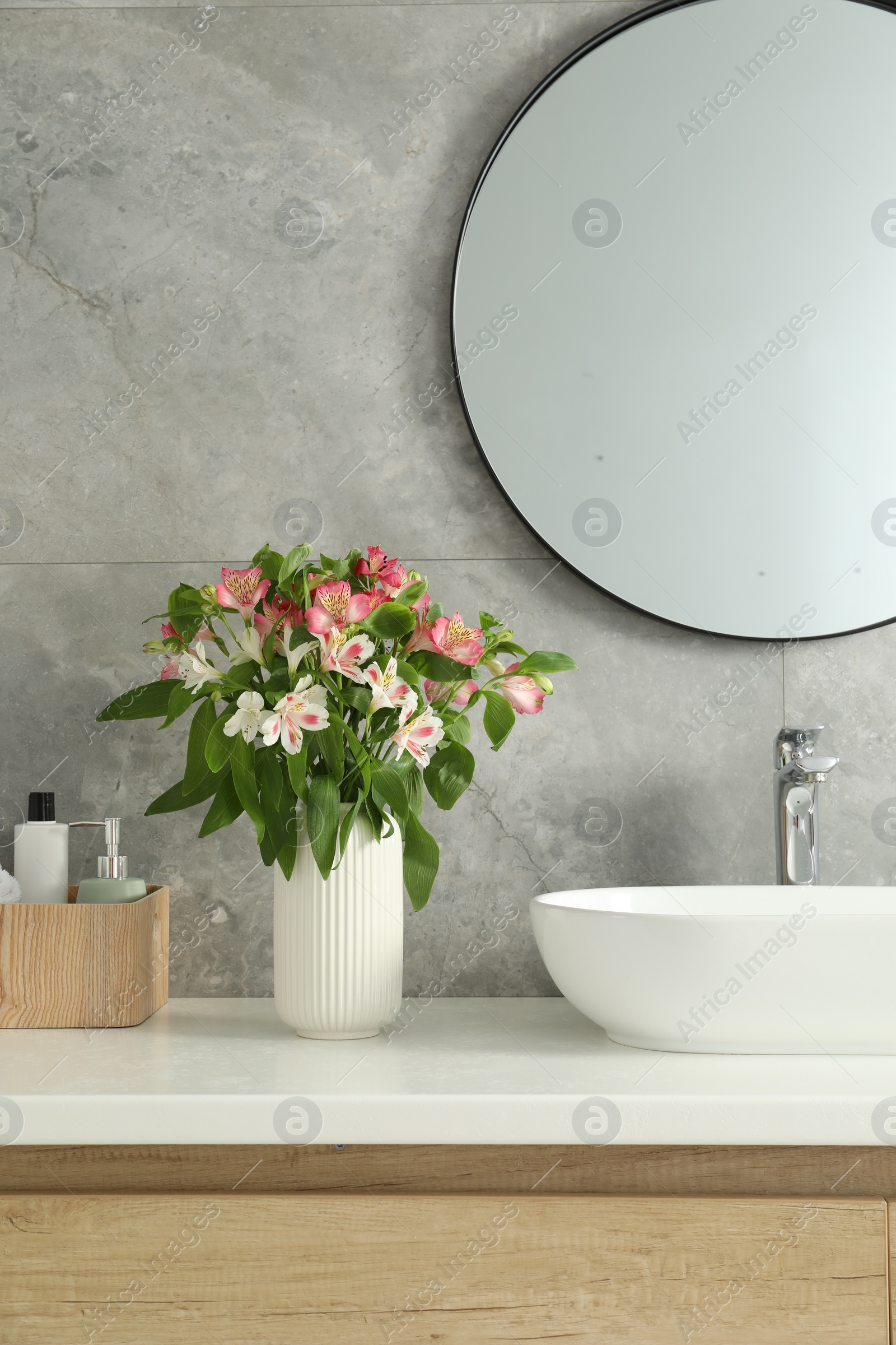 Photo of Vase with beautiful Alstroemeria flowers and toiletries near sink in bathroom