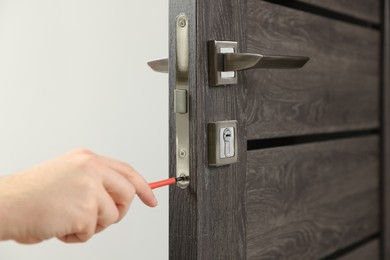 Photo of Worker with screwdriver repairing door lock indoors, closeup