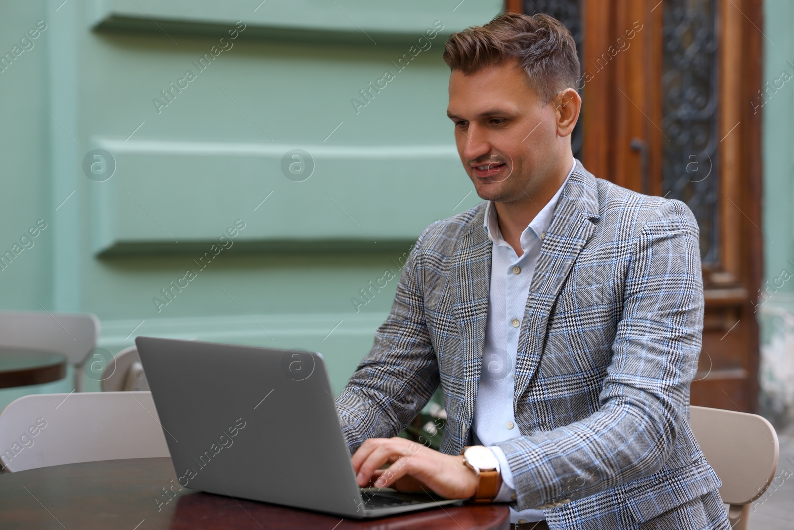 Photo of Handsome man working on laptop at table in outdoor cafe