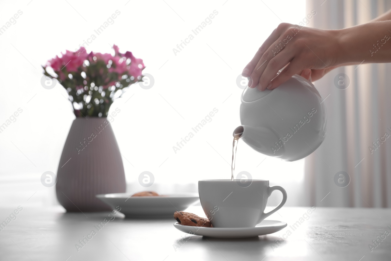 Photo of Woman pouring hot tea into cup at table, closeup