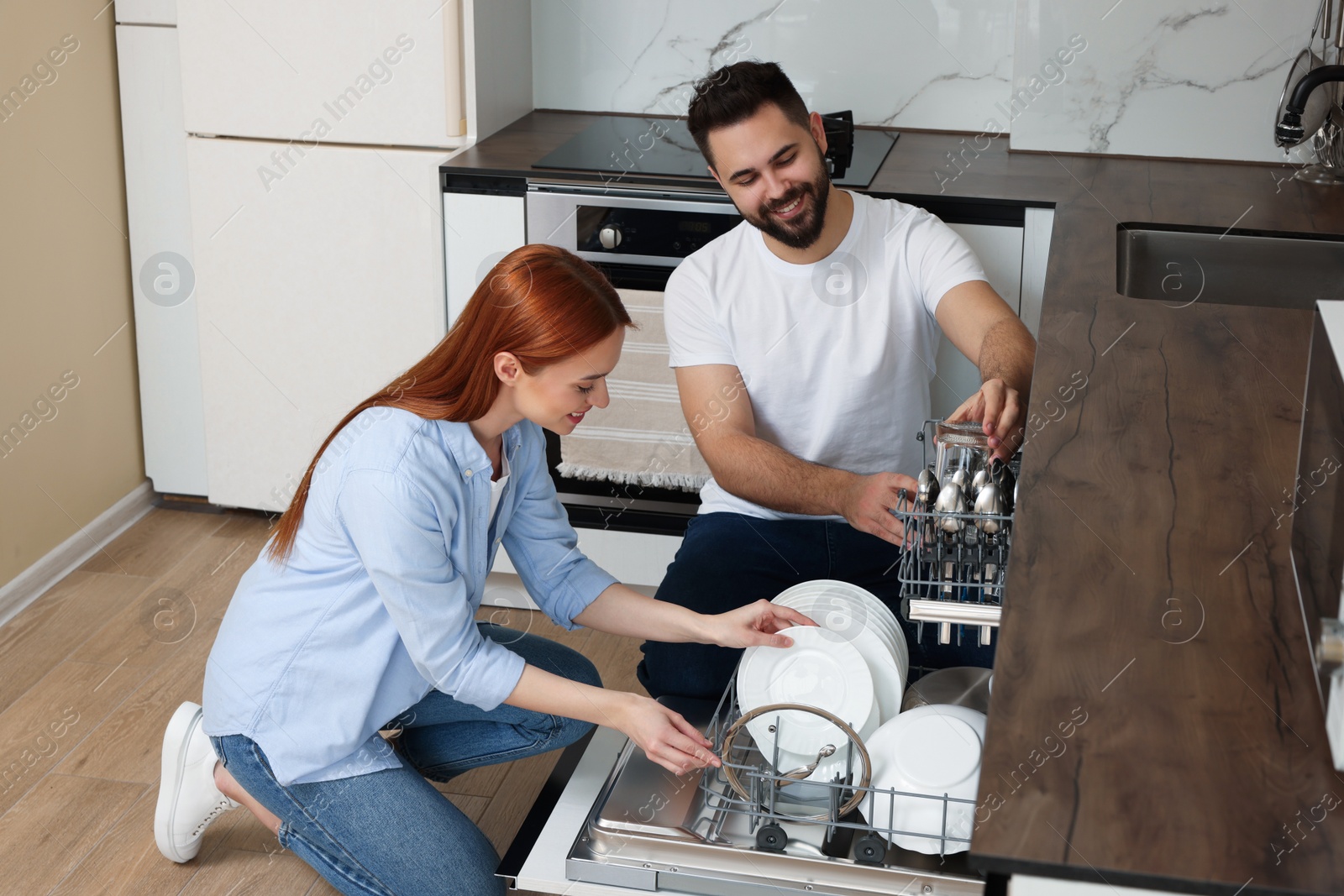 Photo of Happy couple loading dishwasher with plates in kitchen