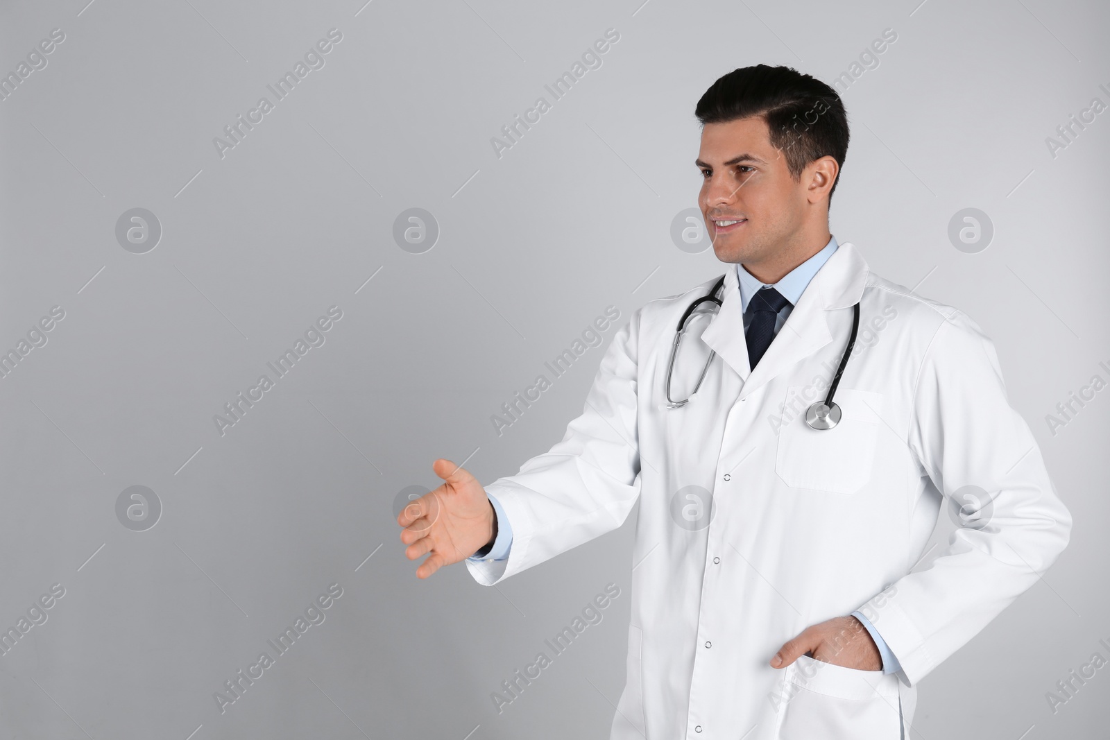 Photo of Happy male doctor offering handshake on light grey background. Space for text
