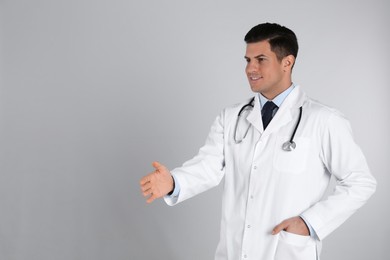 Happy male doctor offering handshake on light grey background. Space for text