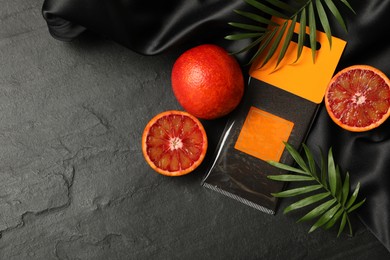 Photo of Scented sachet, red oranges and leaves on black table, flat lay. Space for text