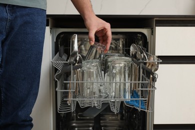Photo of Man loading dishwasher with glass and cutlery indoors, closeup