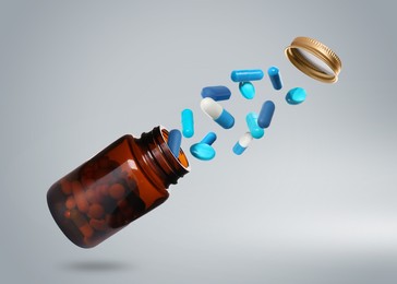 Image of Many different colorful pills bursting out of bottle on light grey background