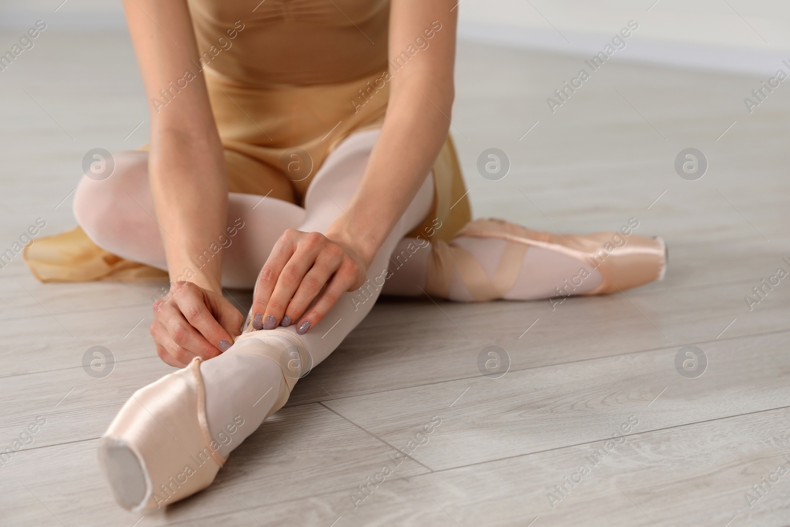 Photo of Ballerina tying pointe shoes on floor in dance studio, closeup. Space for text