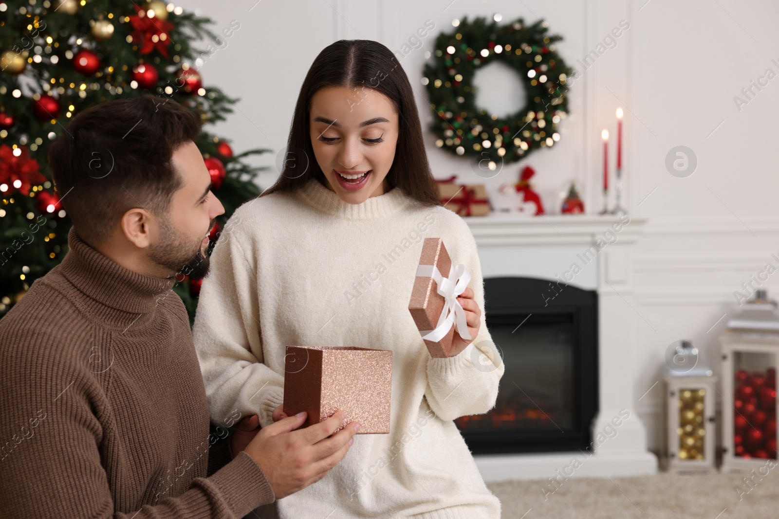 Photo of Surprised young woman opening Christmas gift from her boyfriend at home