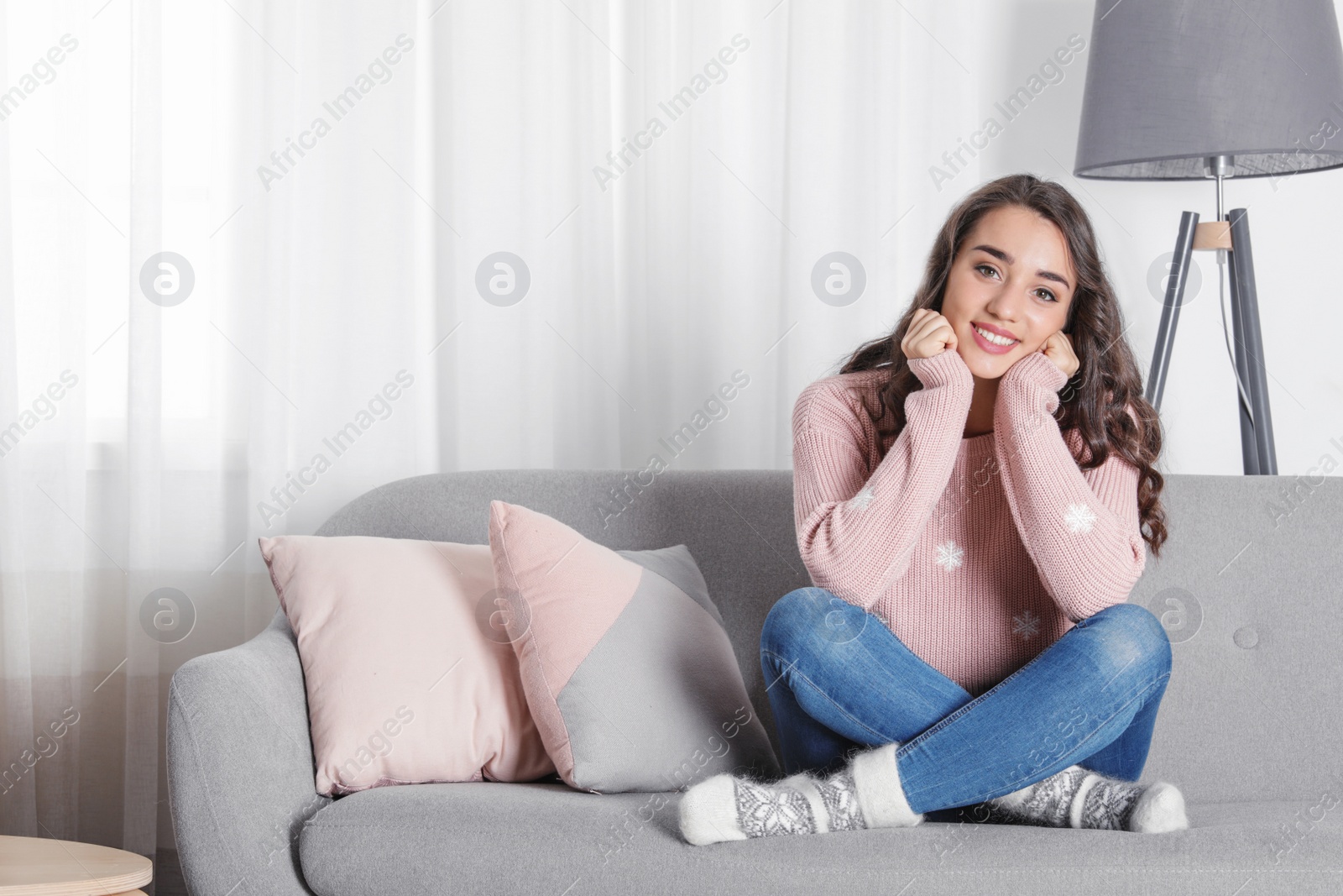 Photo of Young woman in warm sweater sitting on sofa at home. Space for text