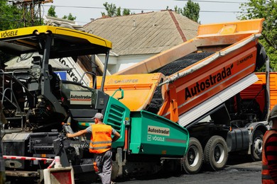 Photo of MYKOLAIV, UKRAINE - AUGUST 04, 2021: Worker with road repair machinery laying new asphalt