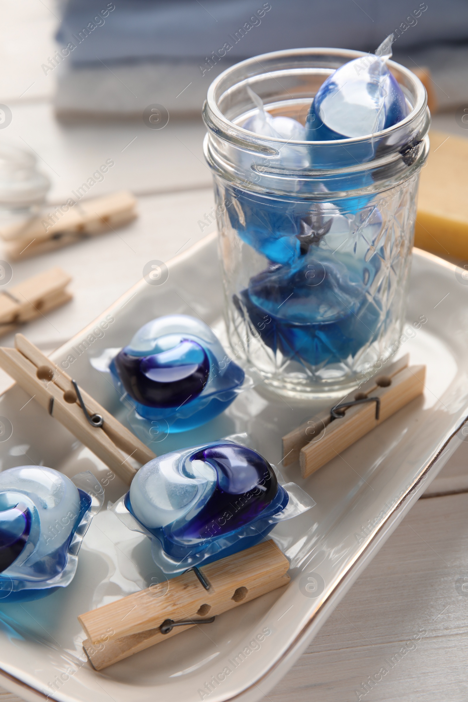 Photo of Many wooden clothespins and laundry detergent pods on white table