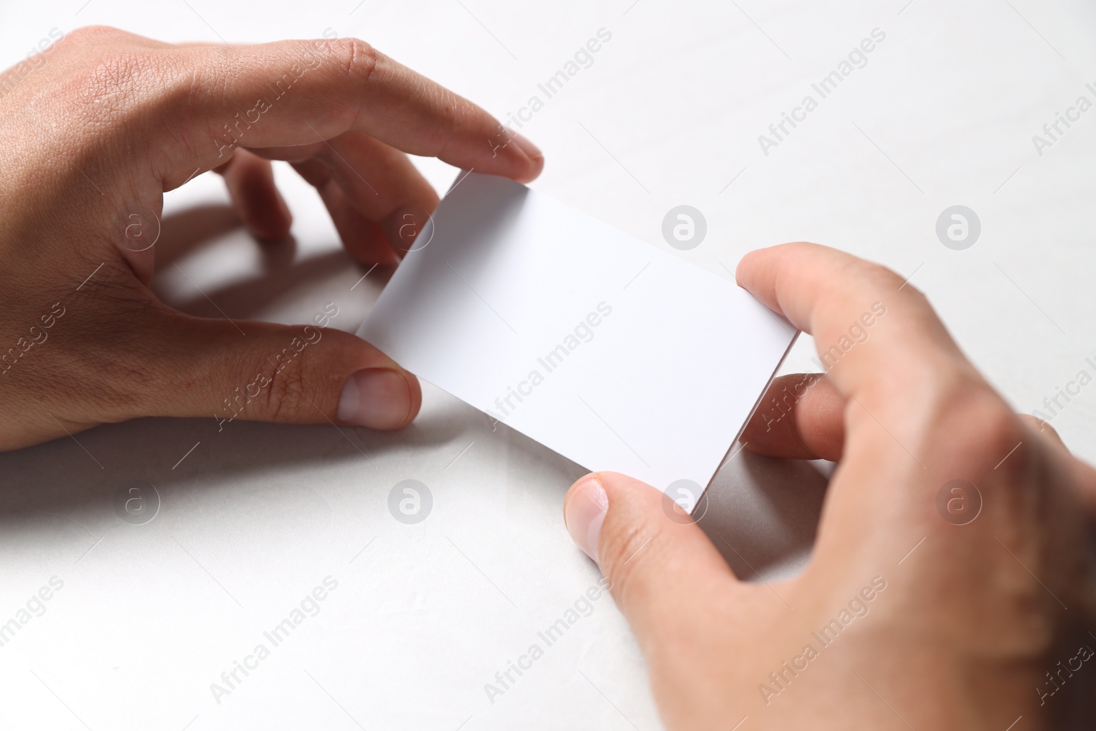 Photo of Man holding blank cards at white table, closeup. Mockup for design