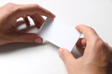 Man holding blank cards at white table, closeup. Mockup for design