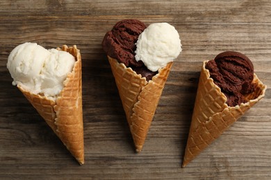 Ice cream scoops in wafer cones on wooden table, flat lay