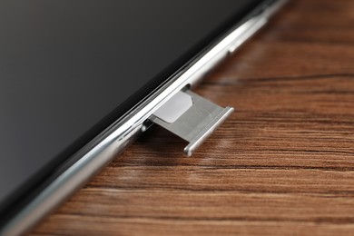 Mobile phone with Sim card in tray on wooden table, closeup